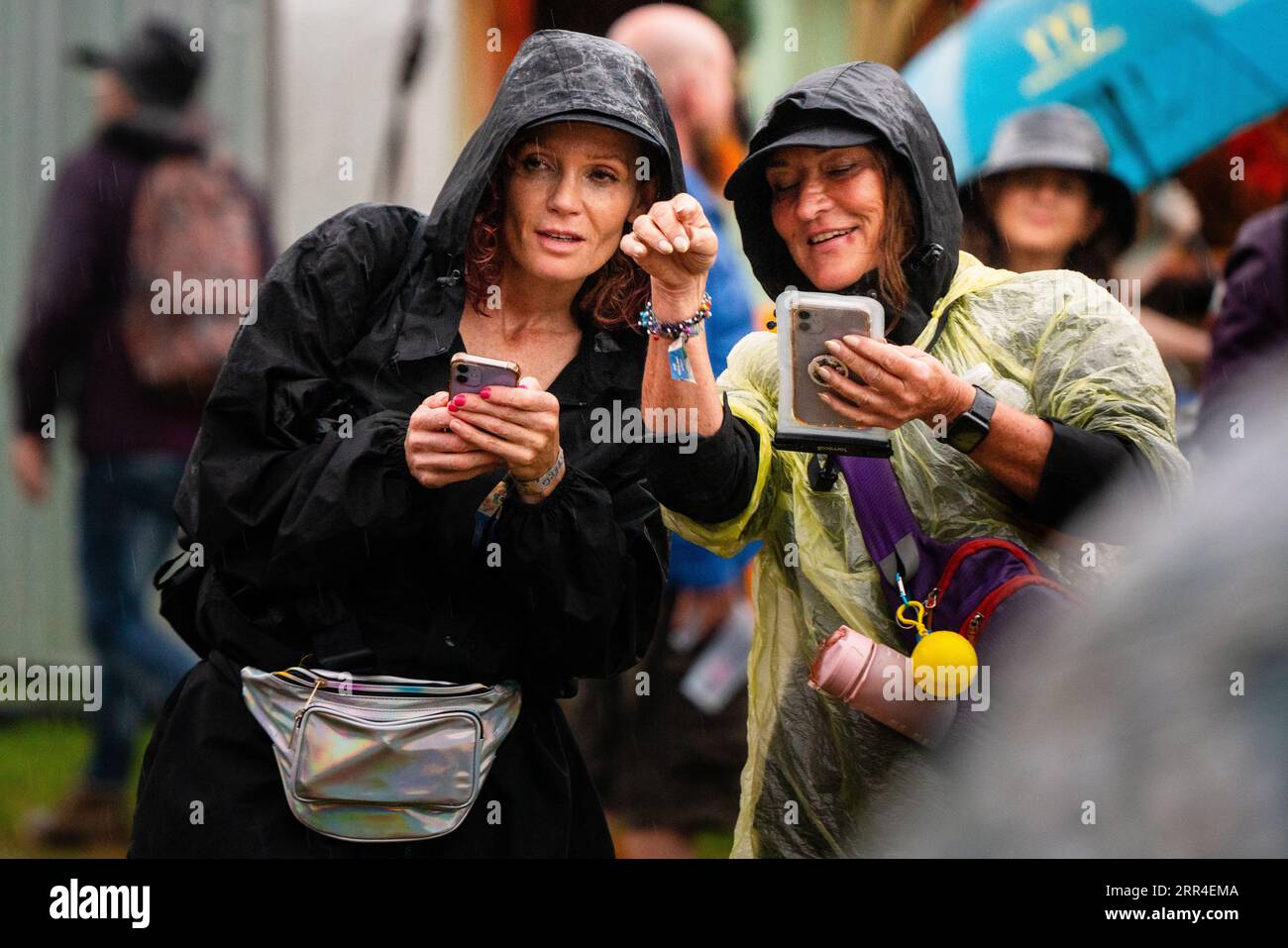 Zwei Frauen in Einweg-Wetten auf ihren Mobiltelefonen im Regen und Schlamm. Green man Festival, Brecon, Wales, Großbritannien, 2023. Foto: Rob Watkins Stockfoto