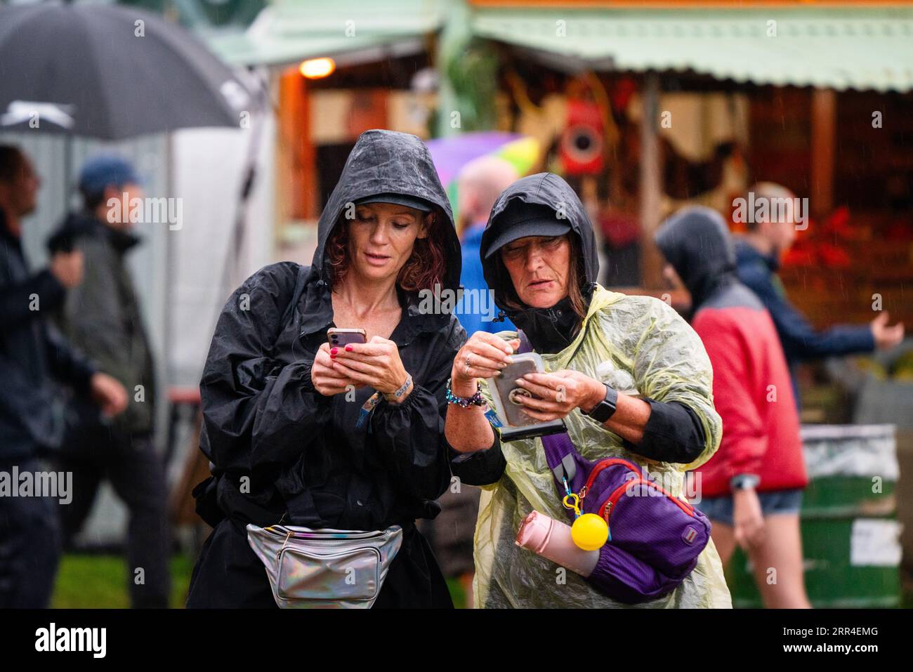 Zwei Frauen in Einweg-Wetten auf ihren Mobiltelefonen im Regen und Schlamm. Green man Festival, Brecon, Wales, Großbritannien, 2023. Foto: Rob Watkins Stockfoto