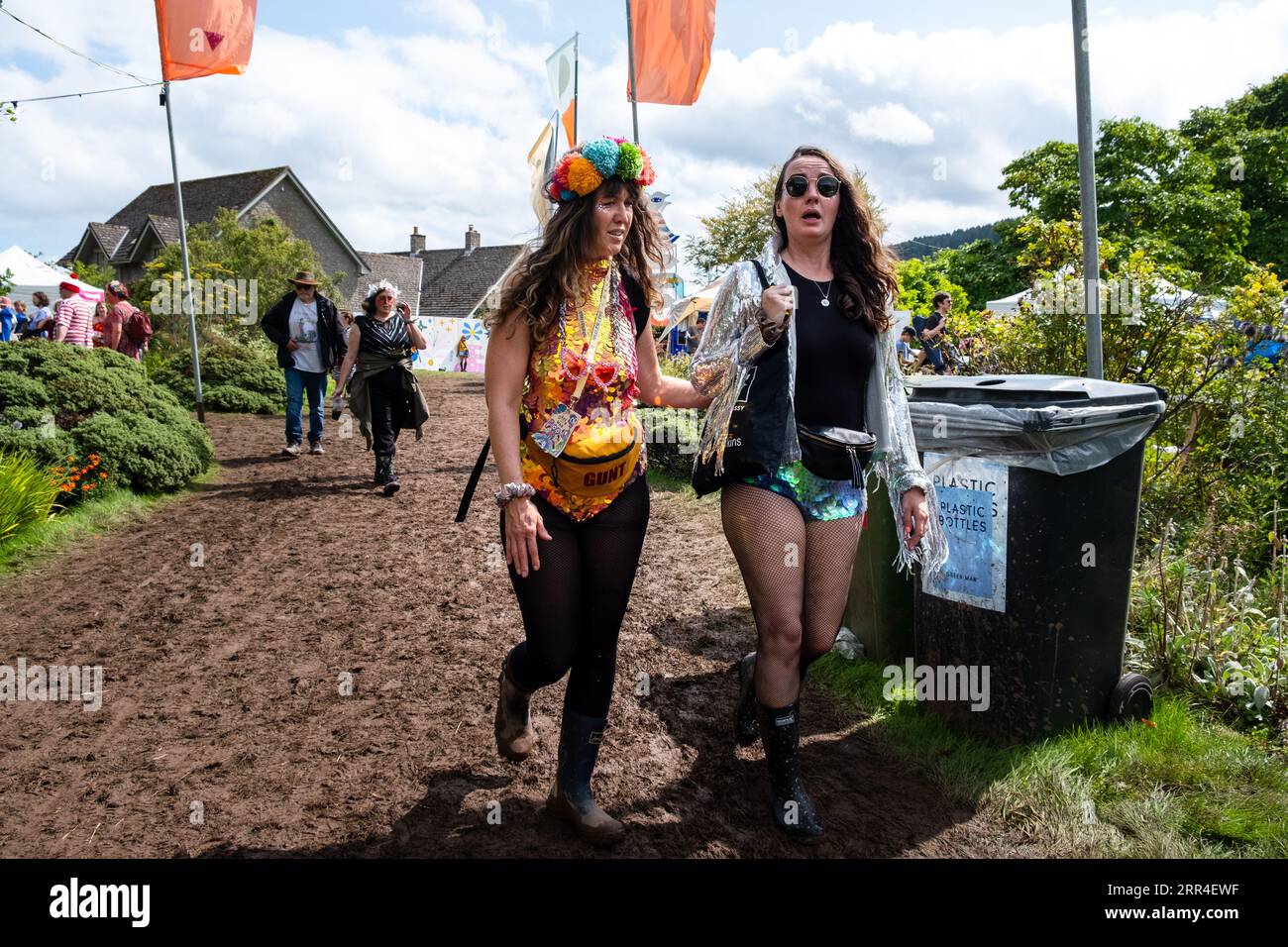 Zwei liebevoll gekleidete Frauen navigieren auf dem Green man Festival, Brecon, Wales, Großbritannien, 2023 durch den Schlamm. Foto: Rob Watkins Stockfoto