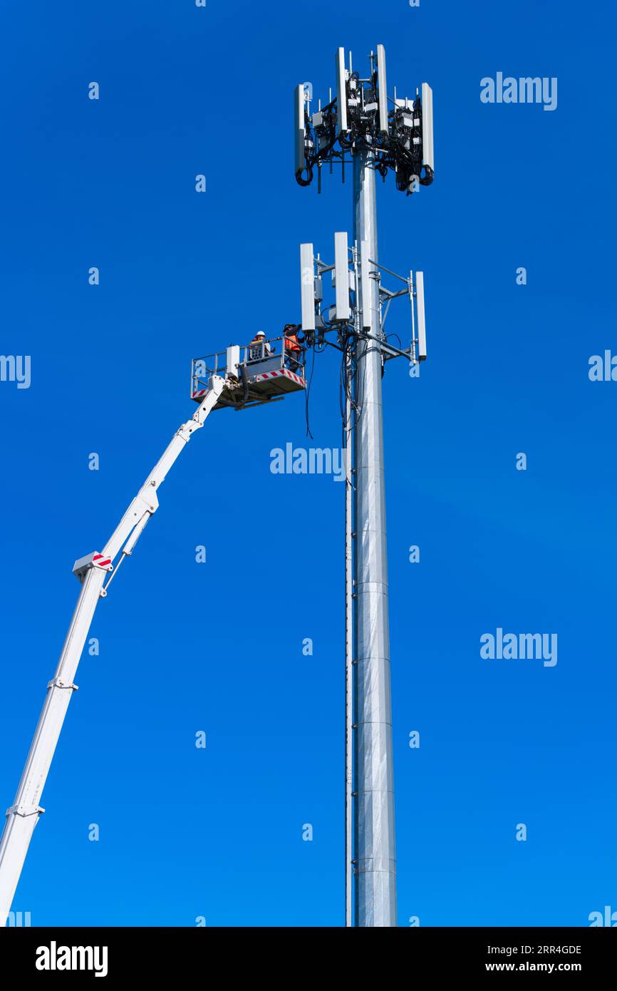 Der Techniker und Arbeiter des Mobilfunkturms führt Reparaturen an einem Mobilfunkturm in Victoria, Australien, mit blauem Himmel durch. Stockfoto