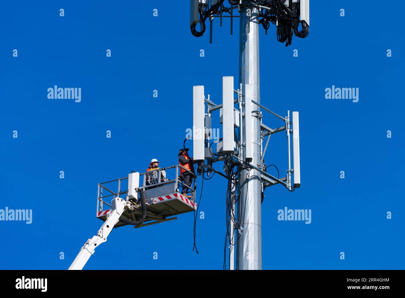 Der Techniker und Arbeiter des Mobilfunkturms führt Reparaturen an einem Mobilfunkturm in Victoria, Australien, mit blauem Himmel durch. Stockfoto