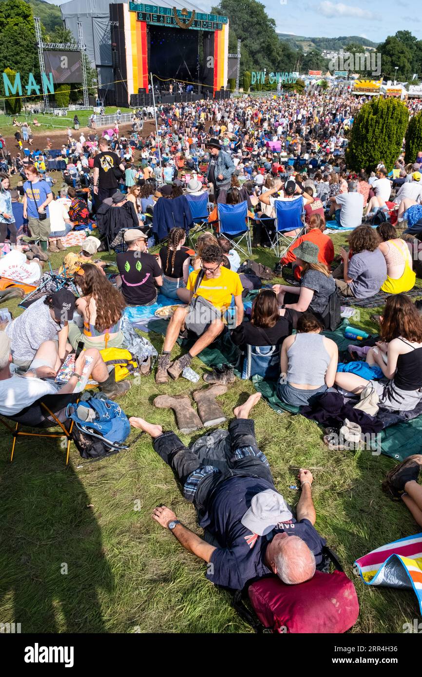 Ein älterer Mann im mittleren Alter macht ein Mittagsschlaf in der Sonne und legt seine matschigen Gummistiefel auf das Gras beim Green man Festival, Brecon, Wales, Großbritannien, 2023. Foto: Rob Wat Stockfoto