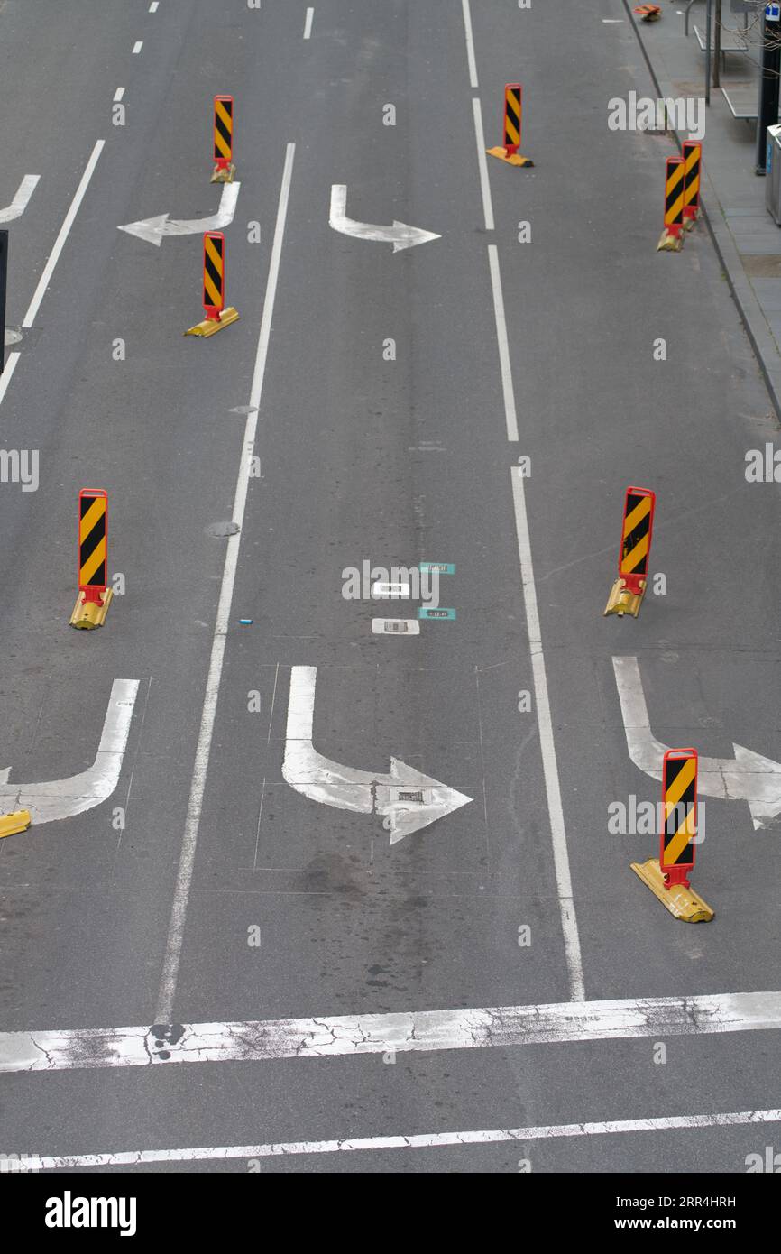 Straßenverkehrskontrolle mit weißen Pfeilen und gestreiften reflektierenden Verkehrskegeln auf Asphaltoberfläche, Melbourne City, Australien. Stockfoto