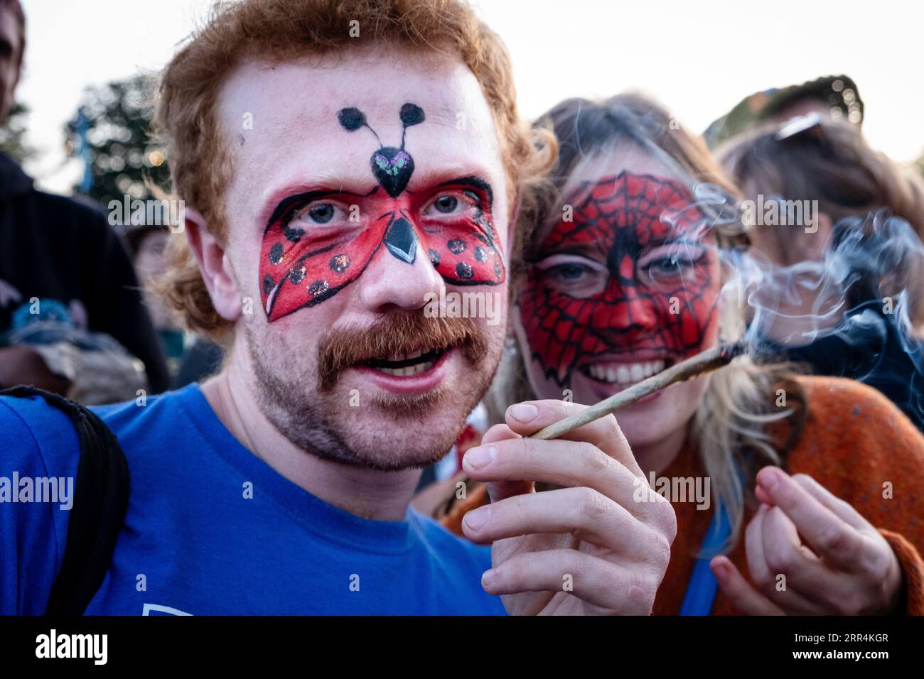 Ein Paar in Face Paint raucht eine riesige Roll-up-Zigarette auf dem Hauptfeld beim Green man Festival, Brecon, Wales, Großbritannien, 2023. Foto: Rob Watkins Stockfoto