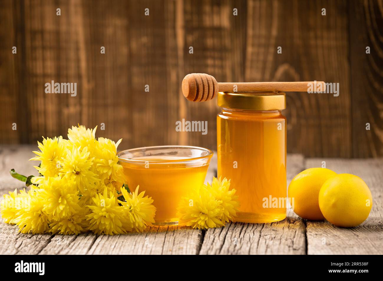 Blume Honig in einem Glas und Schüssel, Holzdipper, frische Zitronen auf einem hölzernen Hintergrund. Produkte, die das Immunsystem stärken. Stockfoto