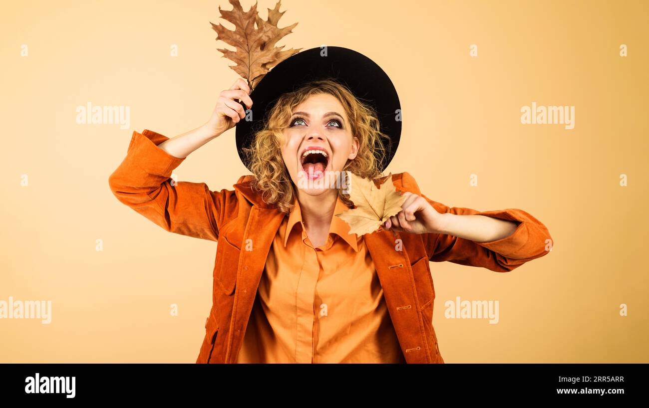 Herbstmodemodell mit schwarzem Hut. Aufgeregtes Mädchen in modischer Kleidung mit gelbem Blatt. Herbstkleidung für Damen. Glückliche Frau in oranger Jacke mit Stockfoto