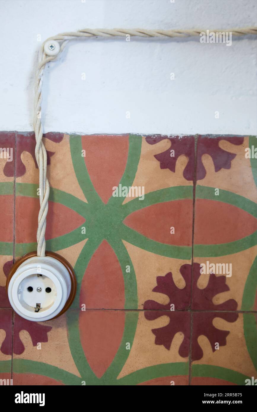 Einzelsteckdose im Vintage-Stil aus Porzellan und Holz über trockener Steinwand. Wiederverwendete Zementfliesen auf Sockelleisten Stockfoto