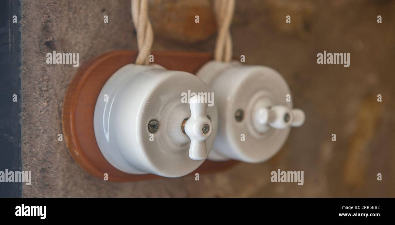 Doppellichtschalter im Vintage-Stil aus Porzellan und Holz über trockener Steinwand. Warmes Licht Stockfoto