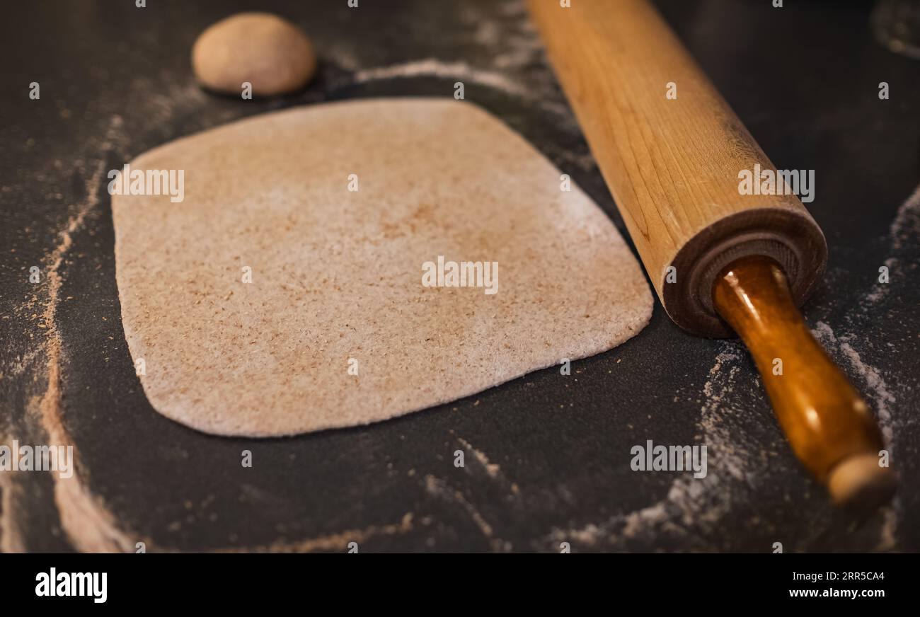 Ausgerollter Vollkornteig, Weizen, Korn mit Vintage-Rollnadel auf dem Tisch. Hausgemachter Bio-Teig. Gerollter Teig auf dem Tisch. Stockfoto