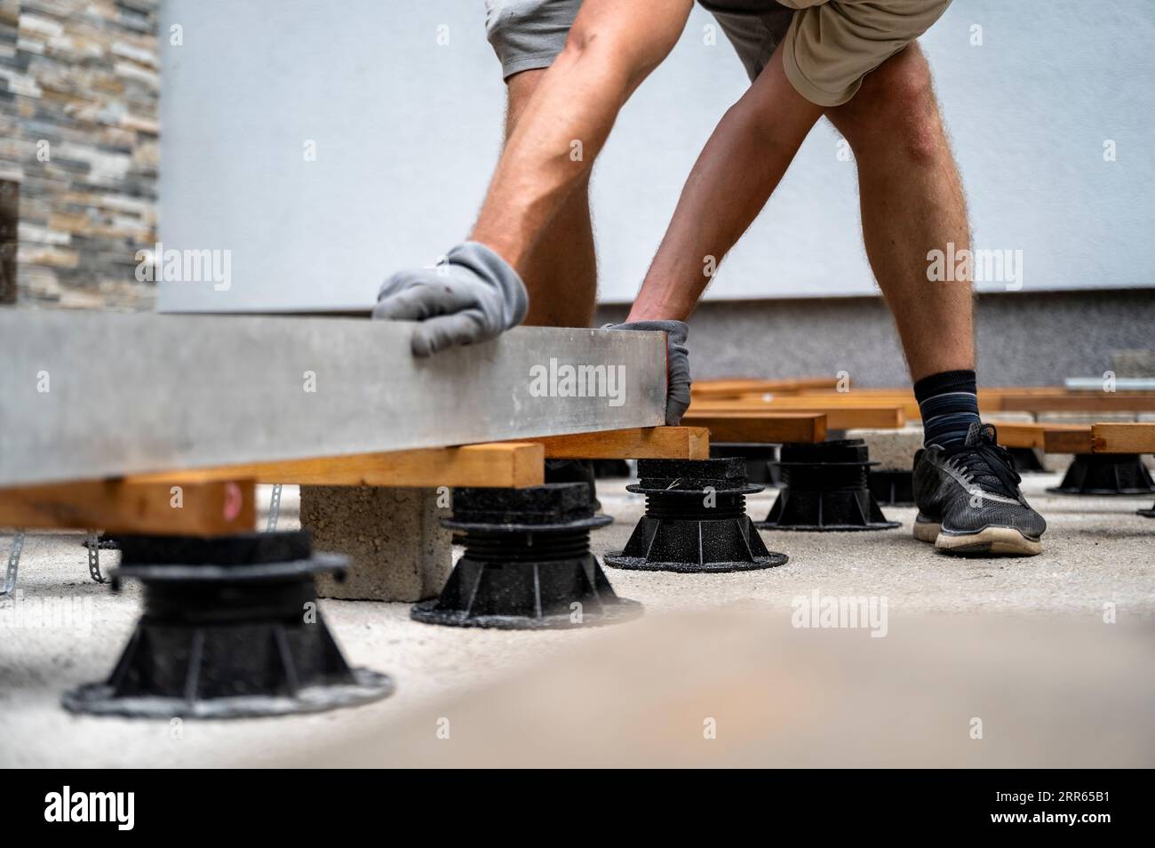 Blick aus einem niedrigen Winkel auf einen Mann, einen Arbeiter, der eine unterstützende Konstruktion für eine Holzterrasse oder Terrasse mit einem langen Etikettenwerkzeug ebnet. Stockfoto