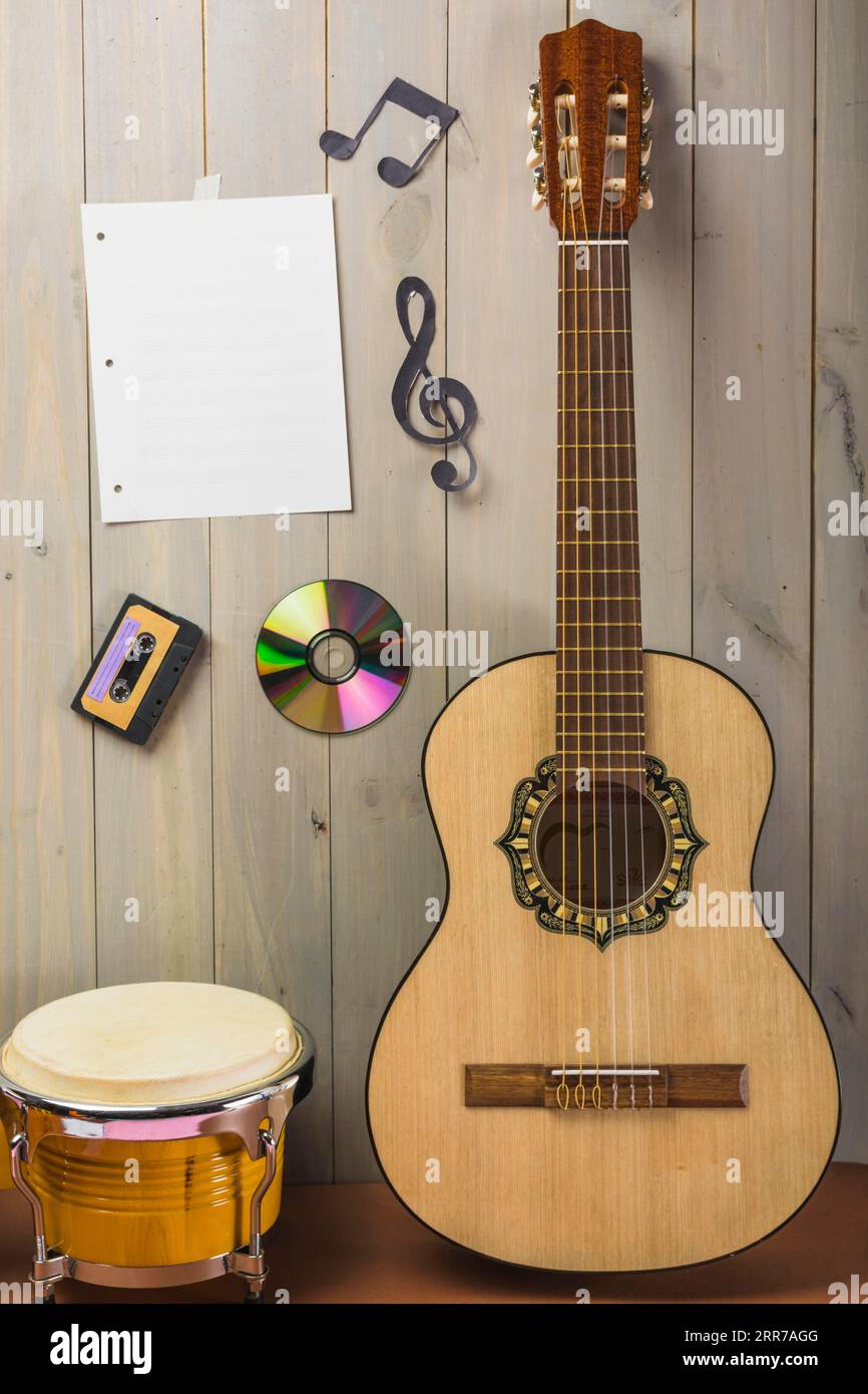 Leere Musikseite Kassette CD-Musiknotiz mit Holzwand und Gitarren-Bongo-Schlagzeug Stockfoto