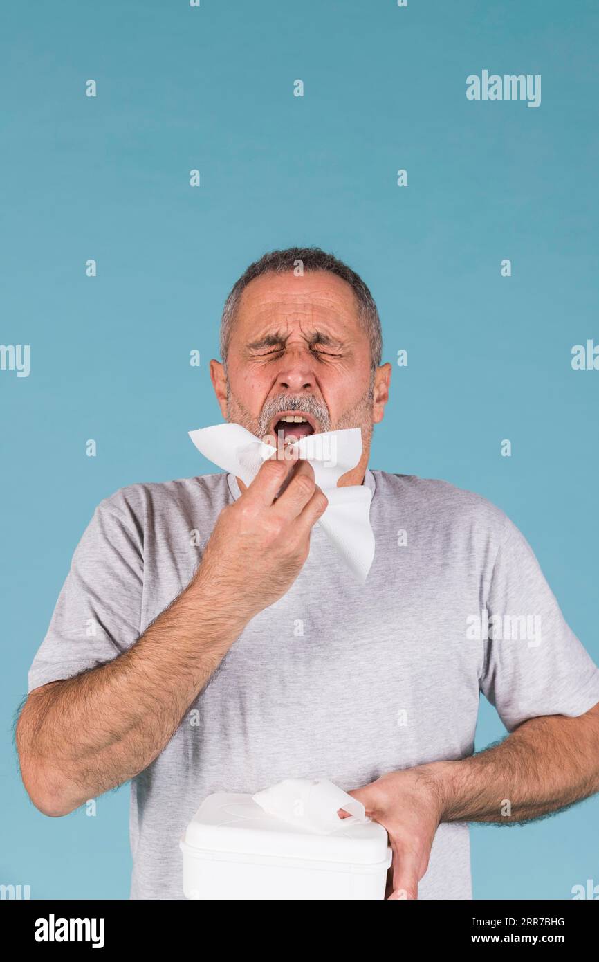 Älterer Mann, der Taschentuch über blauen Nieshintergrund hält Stockfoto