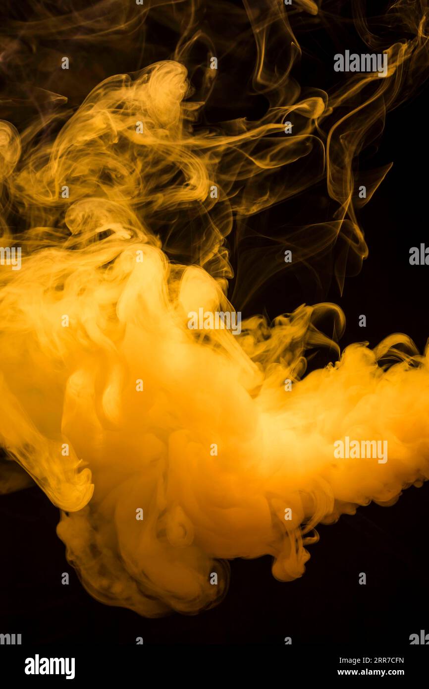 Gelbe helle Rauchwolken breiten sich vor dunkelschwarzem Hintergrund aus Stockfoto