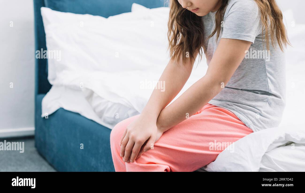 Das Mädchen sitzt im Bett und berührt ihre Knie mit zwei Händen Stockfoto