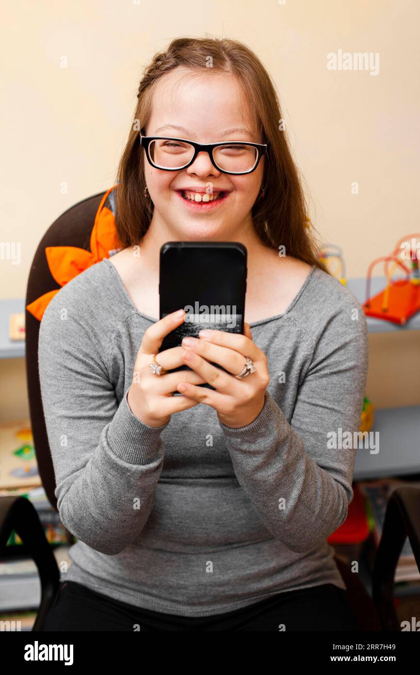 Smiley-Mädchen mit Down-Syndrom, das Telefon hält Stockfoto