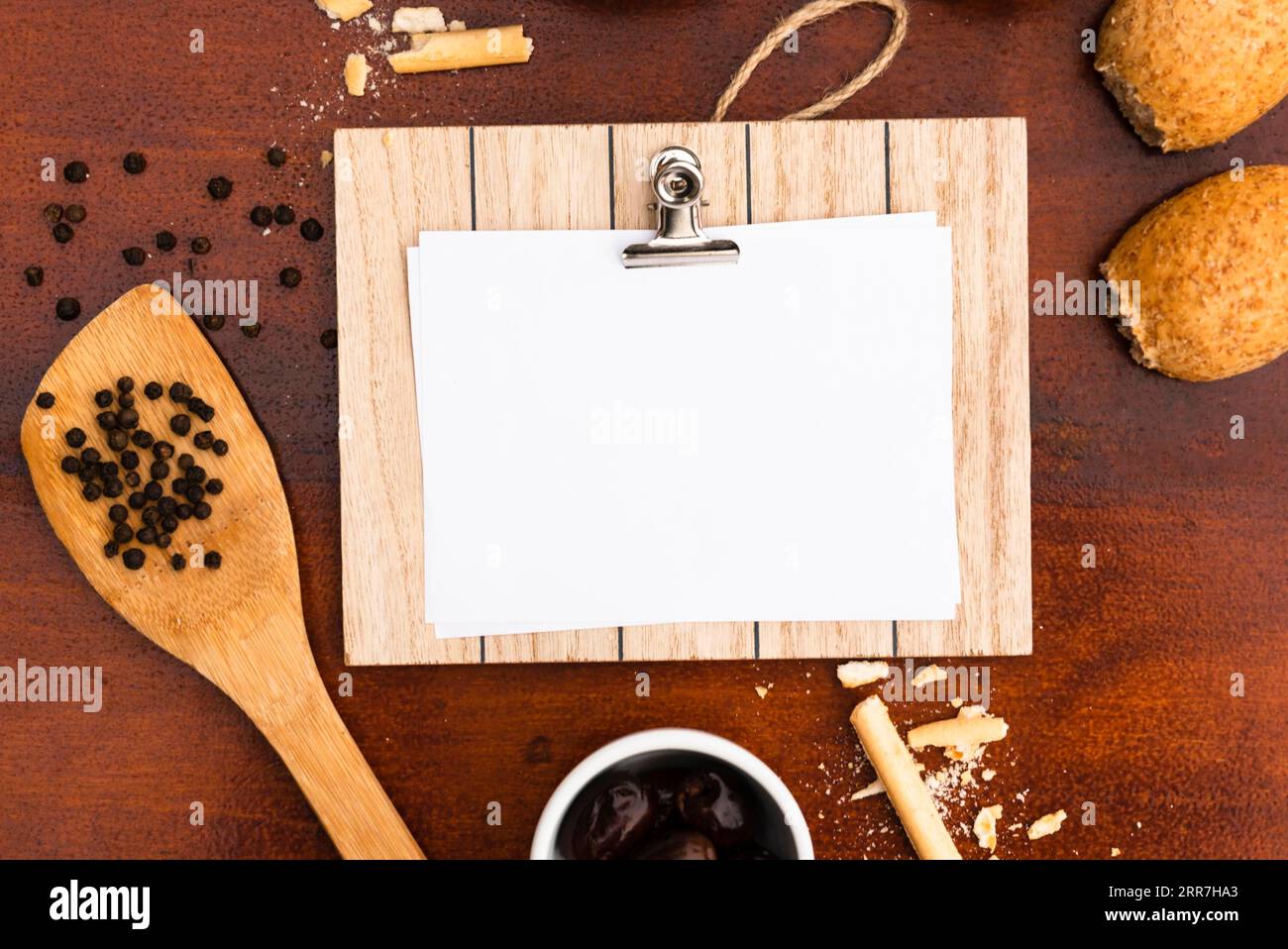 Draufsicht leeres weißes Papier mit Klemmbrett, Brotstangen, Pfeffermais und Spatel, Holzschreibtisch Stockfoto