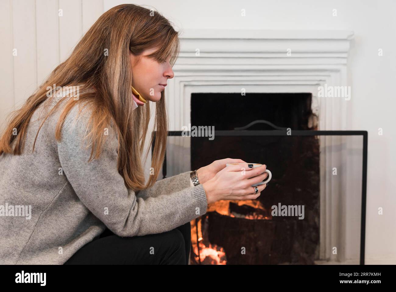 Frauenpullover trinkt Tee in der Nähe des Kamins Stockfoto