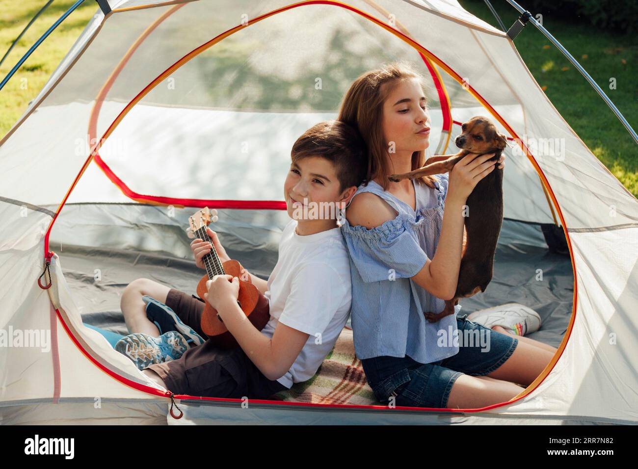 Porträtjunge, sitzendes Zelt mit Hundeschlittenukulele Stockfoto