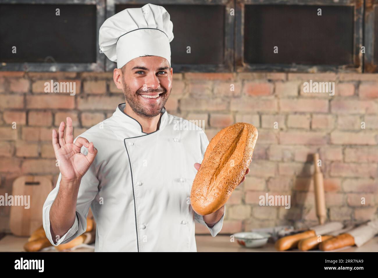 Lächelnder Bäcker, der ein Brot hält und eine Geste mit einem guten Handzeichen zeigt Stockfoto