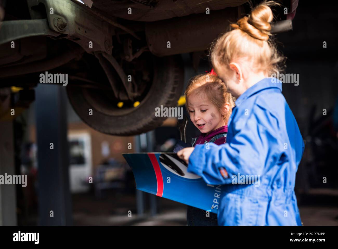 Zwei kleine Mädchen-Overalls mit Schraubenschlüssel-Lesemagazin Stockfoto