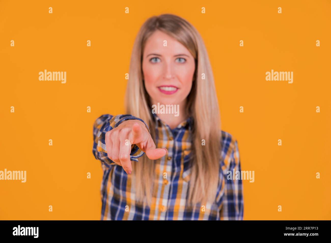 Junge Frau, die mit dem Finger auf die Kamera vor orangefarbenem Hintergrund zeigt Stockfoto