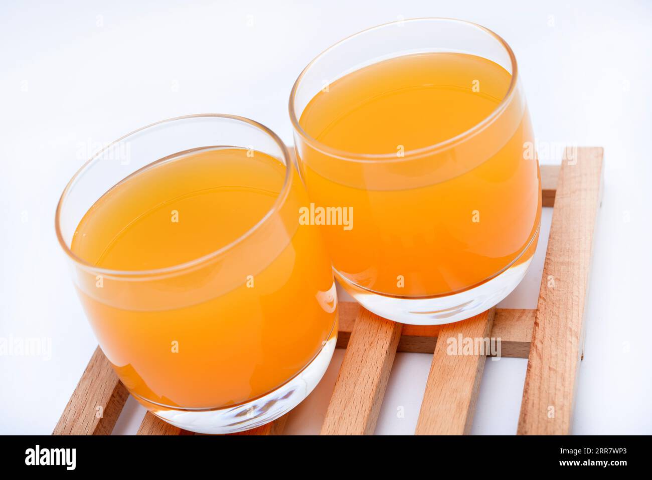 Glasgläser mit Orangensaft auf einem Holzständer. Ein alkoholfreies Getränk im Glas auf weißem Hintergrund. Stockfoto