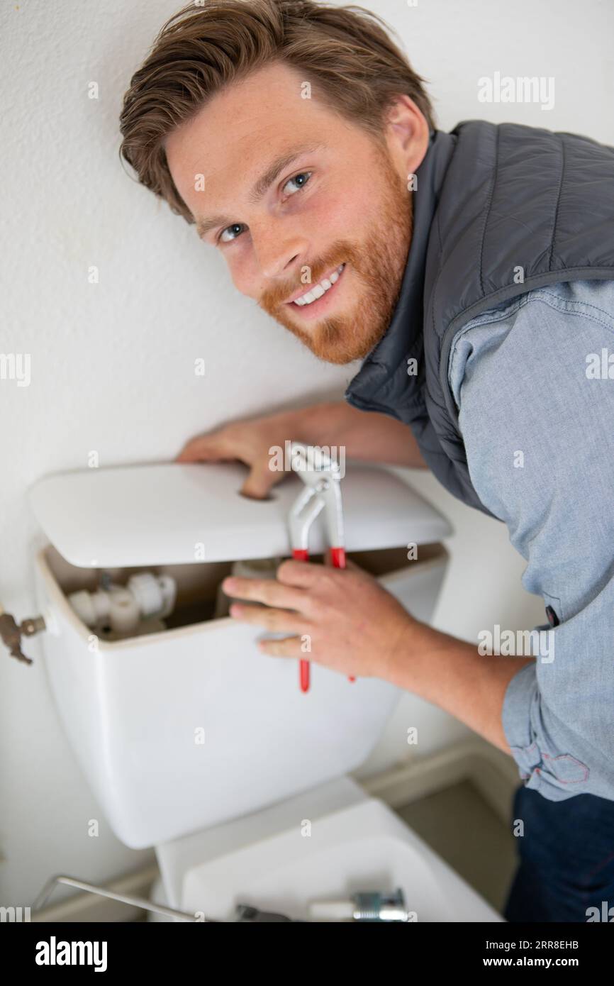 Glücklicher Klempner, der die Toilettenzisterne am Wasserschrank repariert Stockfoto