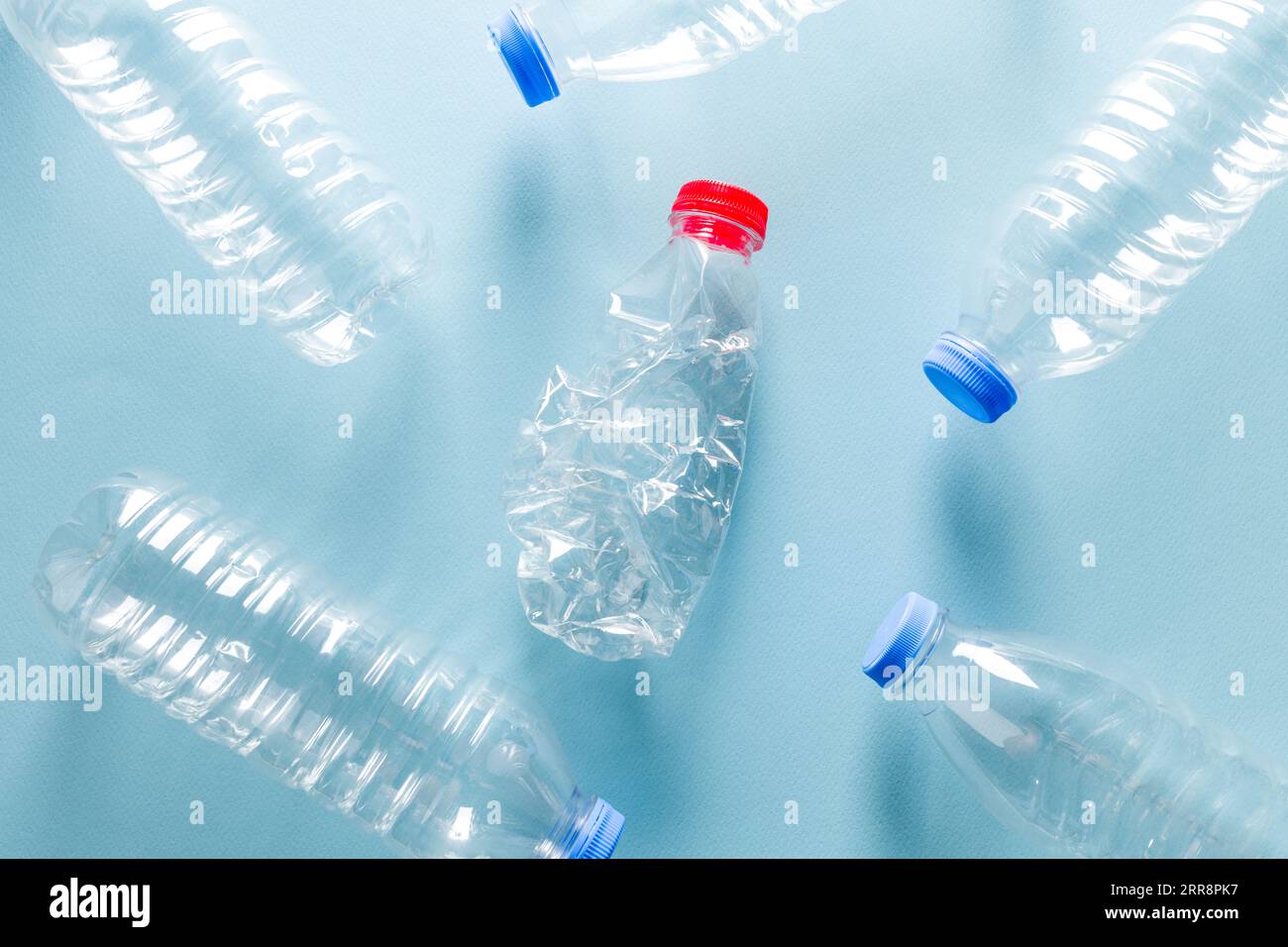 Wasserflaschen aus zerstoßenem Kunststoff mit blauen Kappen, die um die Wasserflasche aus zerstoßenem Kunststoff mit rotem Verschluss auf blauem Hintergrund stehen Stockfoto