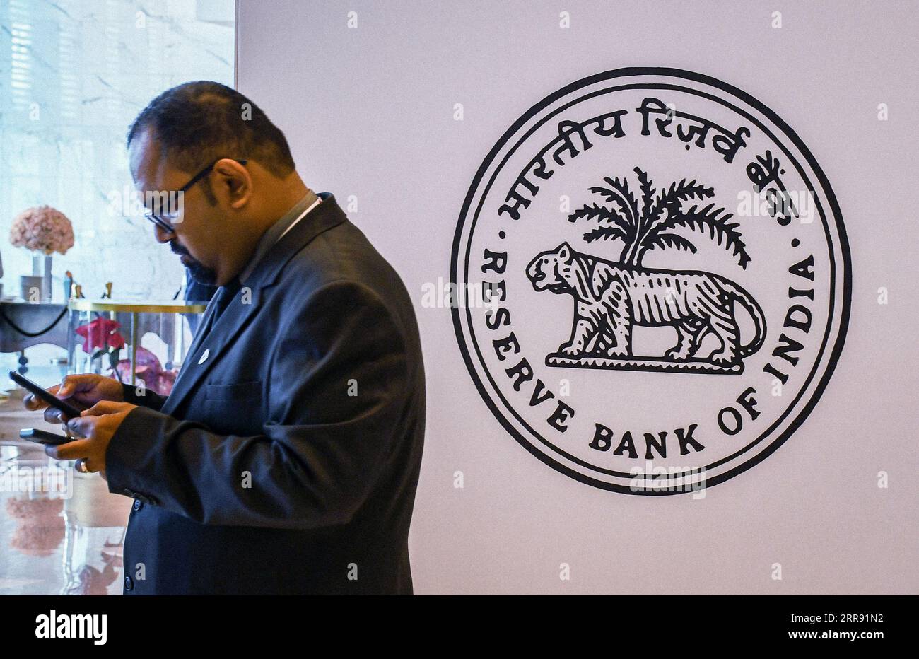 Ein Mann überprüft sein Mobiltelefon in der Nähe des Logos der „Reserve Bank of India“ beim Global Fintech fest (GFF) in Mumbai. Global Fintech fest ist eine weltweite Plattform, auf der sich Interessenvertreter von Fintech-Unternehmen unter einem Dach versammeln, um Ideen, Innovationen, Startups und neue Technologien in den Bereichen Banken, Finanzen und digitale Zahlungen bei einer jährlichen Veranstaltung auszutauschen. (Foto: Ashish Vaishnav/SOPA Images/SIPA USA) Stockfoto