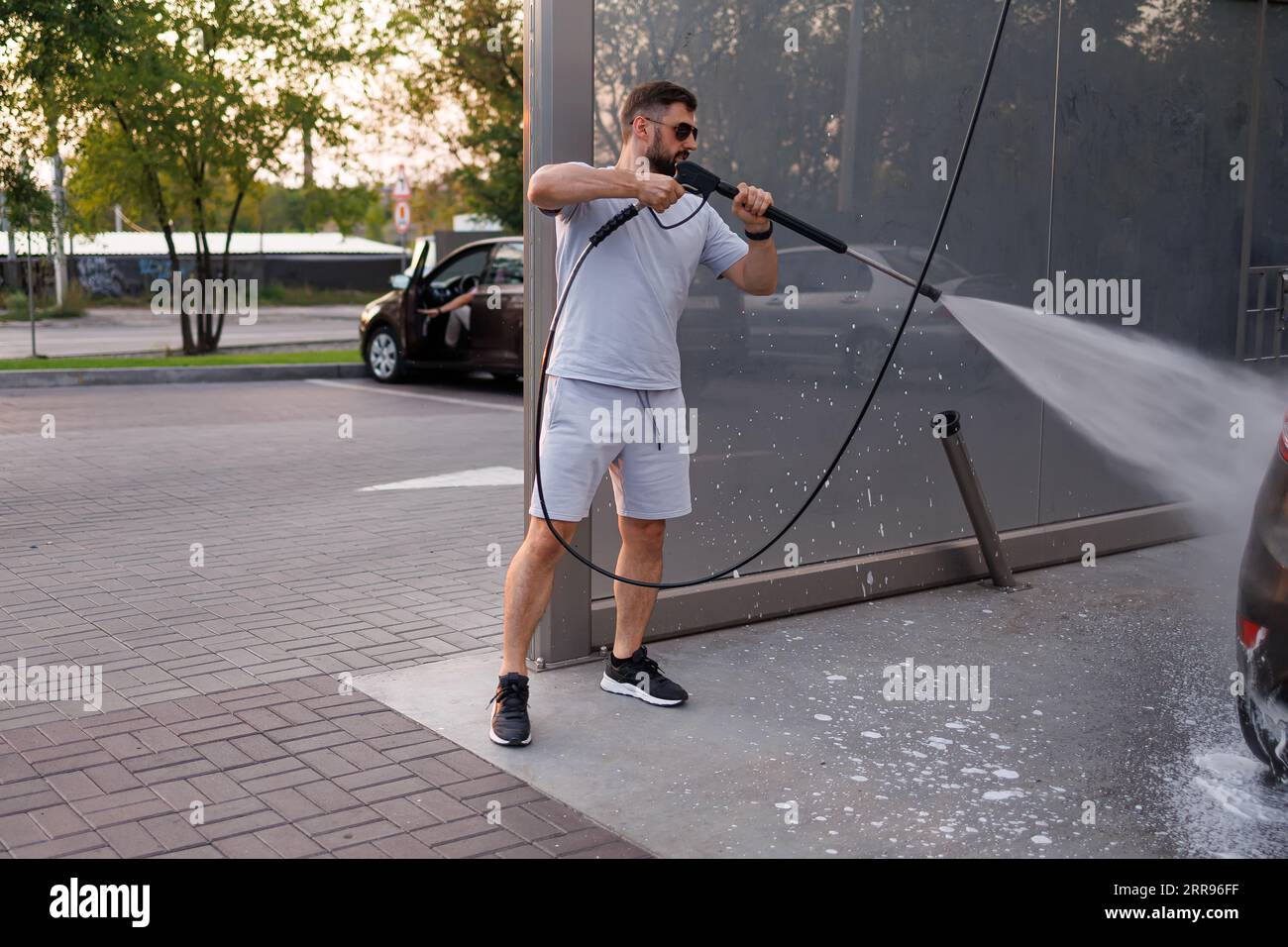 Ein Mann hält eine Wasserkanone, um Ein Auto bei einer Autowaschanlage zu waschen. Stockfoto