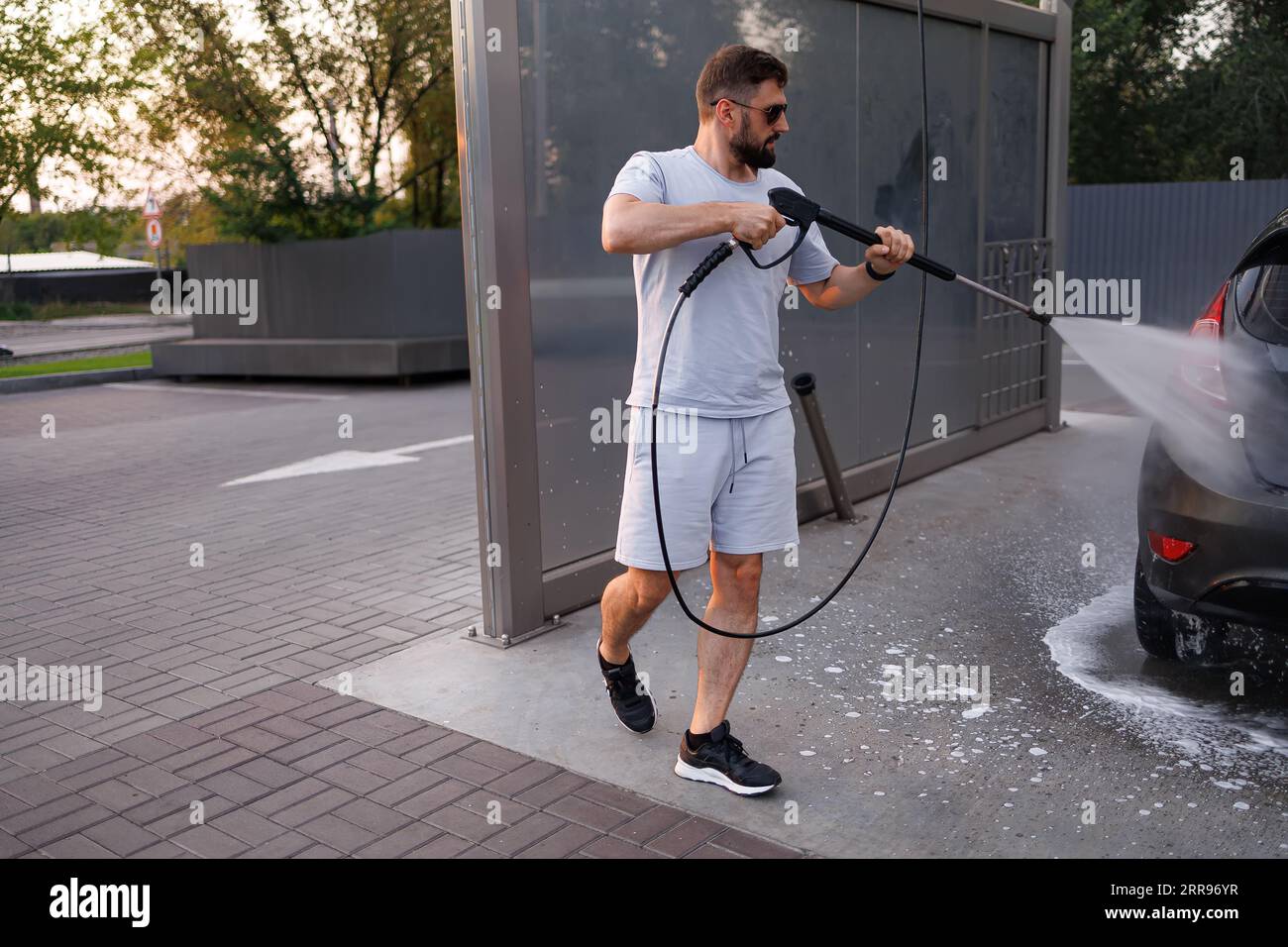 Ein Mann wäscht ein Auto mit einer Wasserkanone, die um es herum läuft. Ein Auto in einer Selbstbedienungswaschanlage. Stockfoto