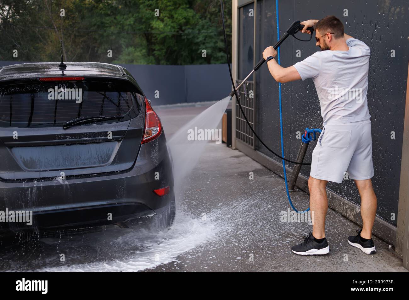 Das Auto ist in einer Autowaschanlage, die von einem Mann mit einer Wasserkanone geleitet wird. Ein Auto in einer Selbstbedienungswaschanlage. Stockfoto