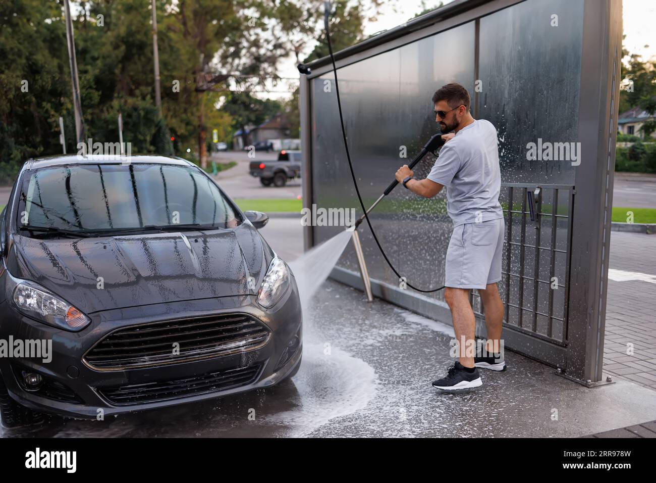 Der vordere Teil des Wagens wird von einem Mann mit einer Wasserkanone gewaschen. Ein Auto in einer Selbstbedienungswaschanlage. Stockfoto
