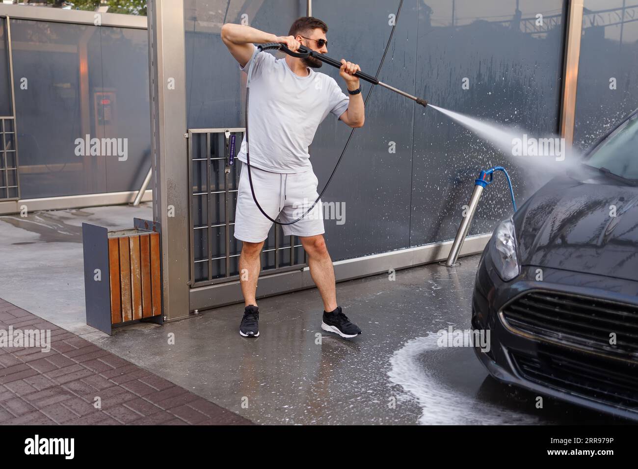 Ein Mann wäscht die Vorderseite eines Autos mit einer Wasserkanone. Ein Auto in einer Selbstbedienungswaschanlage. Stockfoto