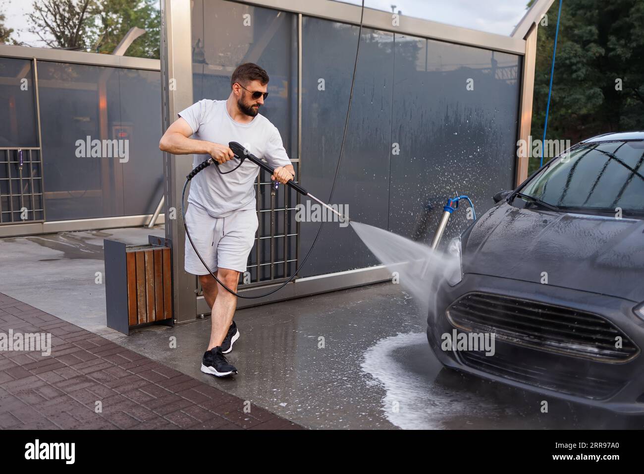Ein Mann wäscht den Frontgrill eines Autos mit einer Wasserkanone. Ein Auto in einer Selbstbedienungswaschanlage. Stockfoto