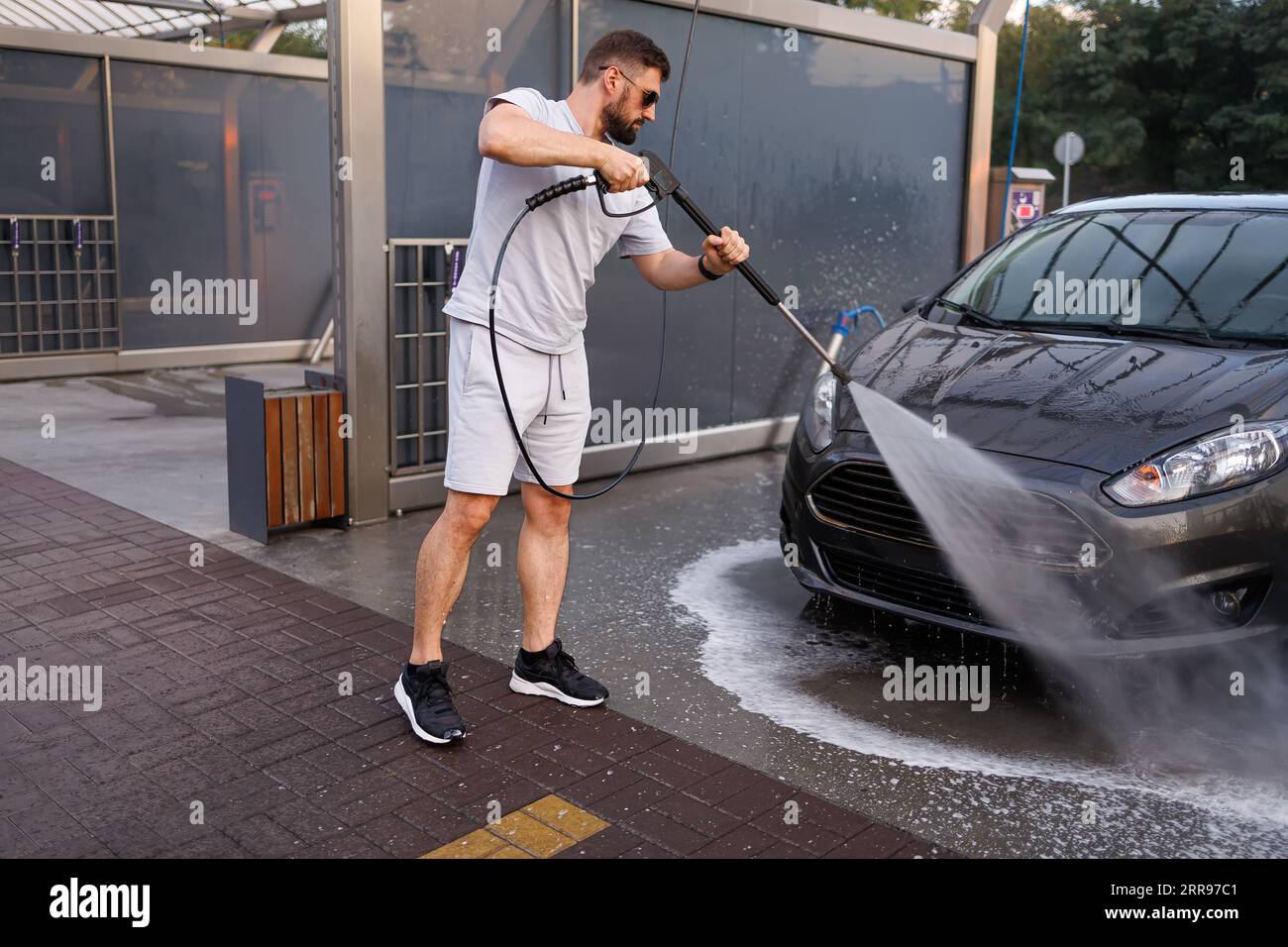 Ein Mann wäscht den Frontgrill eines Autos mit einer Wasserkanone. Ein Auto in einer Selbstbedienungswaschanlage. Stockfoto
