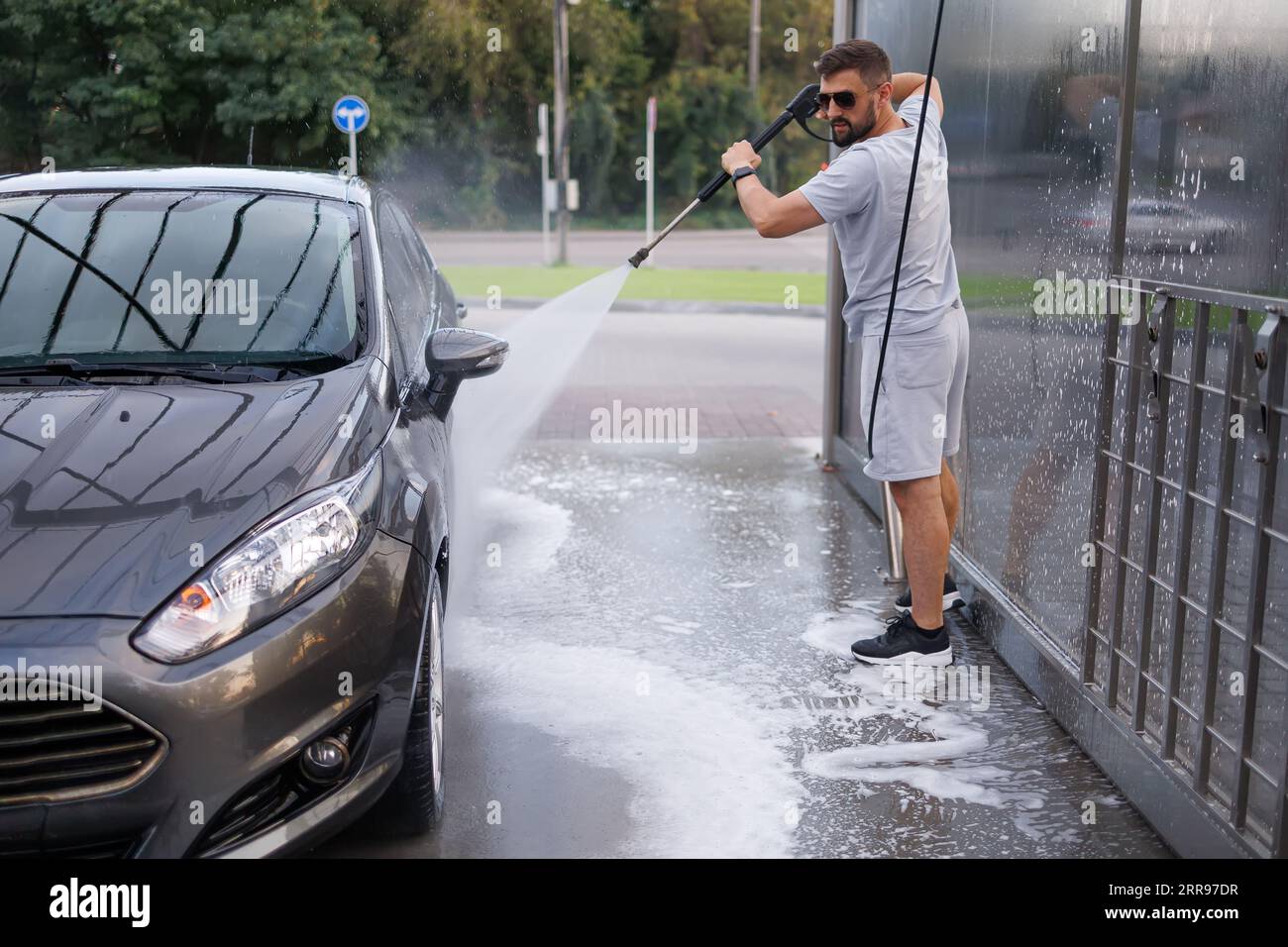 Ein Mann reinigt den Schmutz gründlich mit einer Wasserkanone vom Auto. Ein Auto in einer Selbstbedienungswaschanlage. Stockfoto