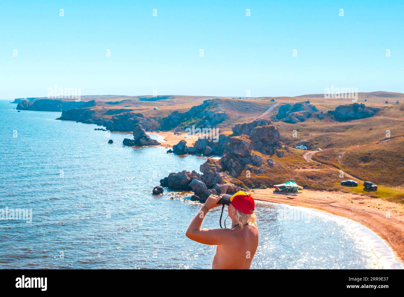 Ein Mann schaut durch ein Fernglas auf die Meereslandschaft. Felsige Küste des Asowschen Meeres, die Strände des Generals. Reise und Tourismus. Stockfoto