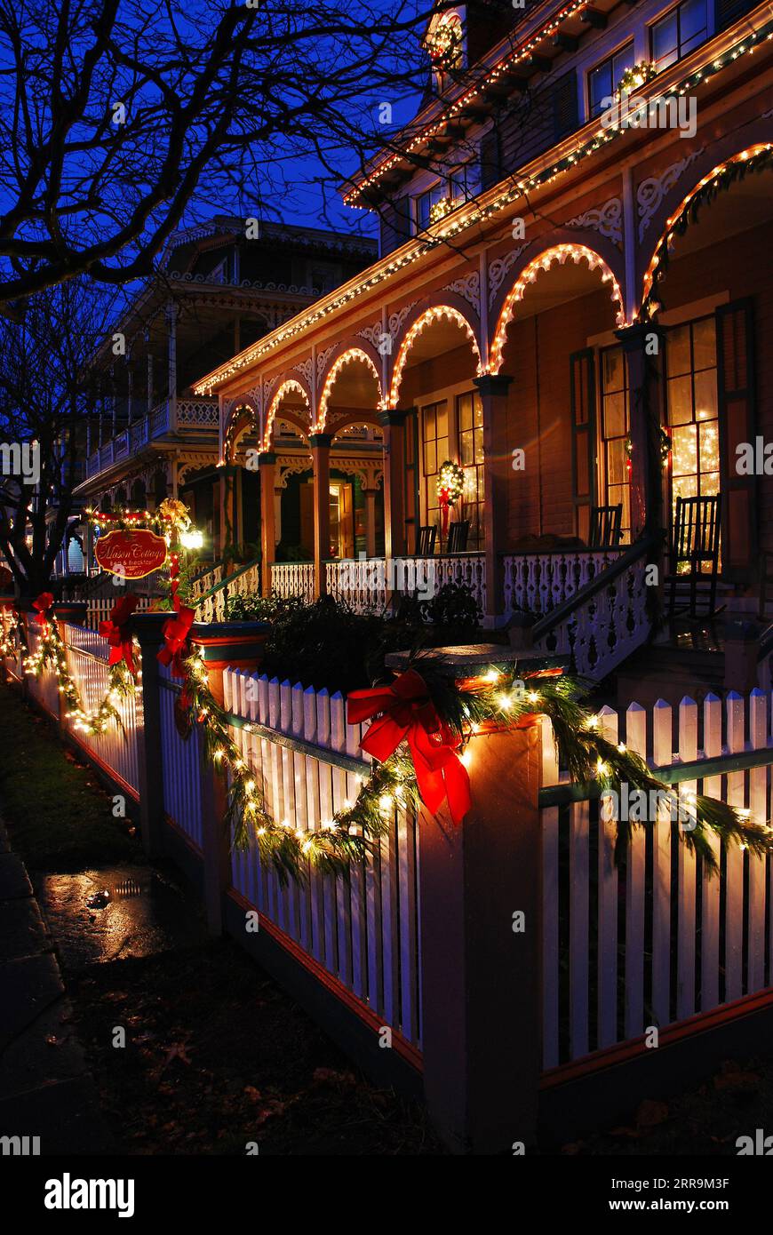 Weihnachtsdekorationen und Lichter, darunter Bögen und stechpalmen, zieren einen weißen Zaun eines viktorianischen Hauses während der Feiertage in Cape May New Jersey Stockfoto