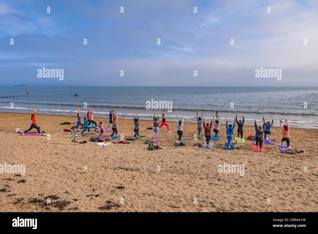 Gruppe von Frauen, die Yoga mit einer Lehrerin am Portobello Beach in Edinburgh, Schottland, Großbritannien, praktizieren. Stockfoto
