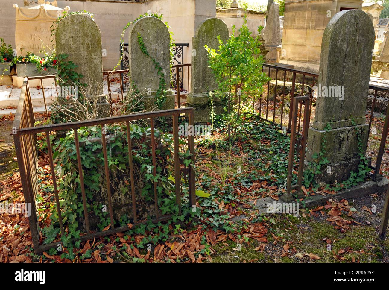 Alte Grabsteine befinden sich auf einem bewachsenen, umzäunten Grabstein auf dem historischen Pariser Friedhof Père Lachaise. Stockfoto