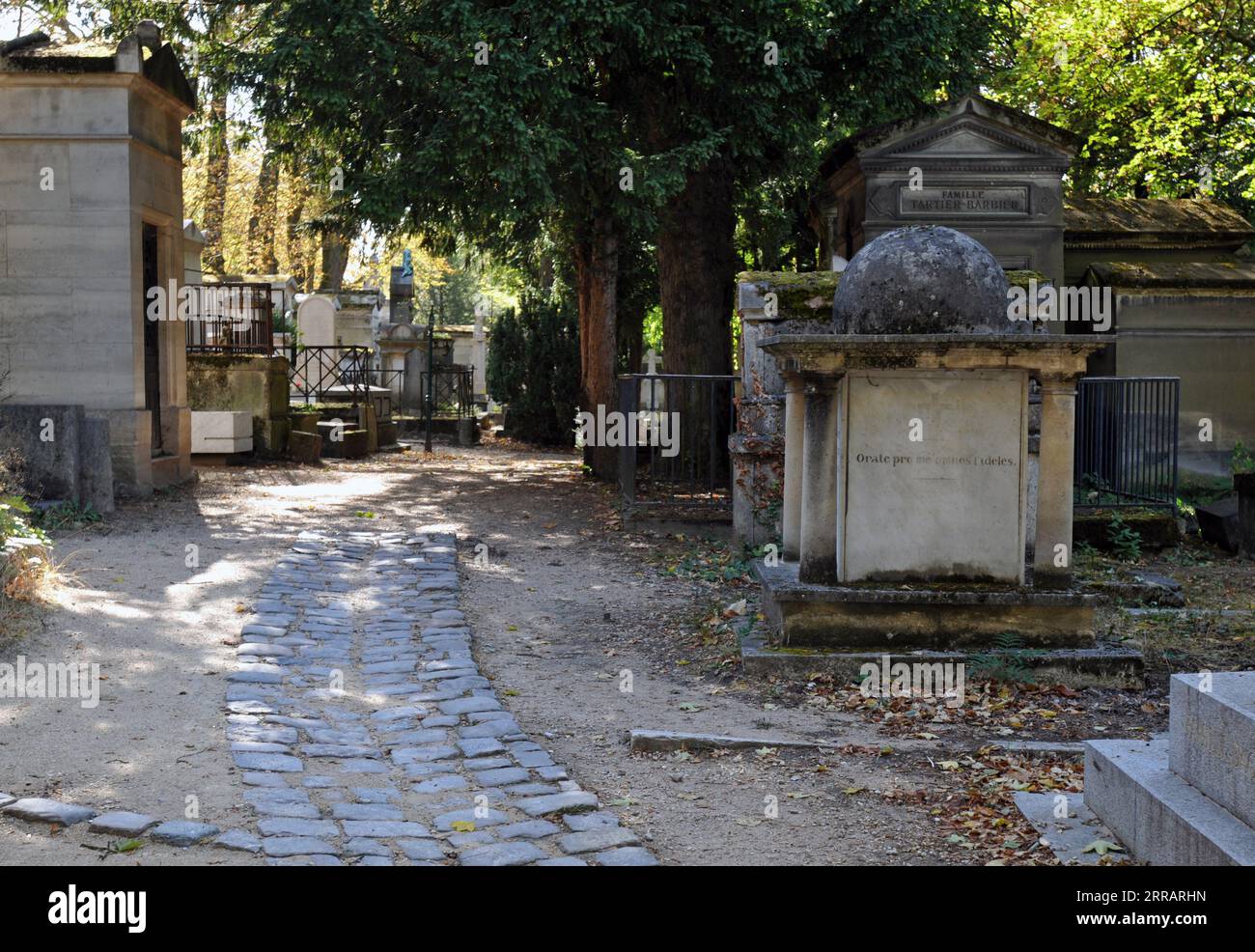 Ein von Bäumen gesäumter Kopfsteinpflasterpfad führt an alten Gräbern und Grabstätten auf dem historischen Pariser Friedhof Père Lachaise vorbei. Stockfoto