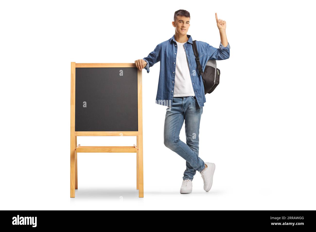 Männlicher Teenager-Student mit einem Rucksack, der sich auf eine kleine Tafel lehnt und isoliert auf weißem Hintergrund nach oben zeigt Stockfoto