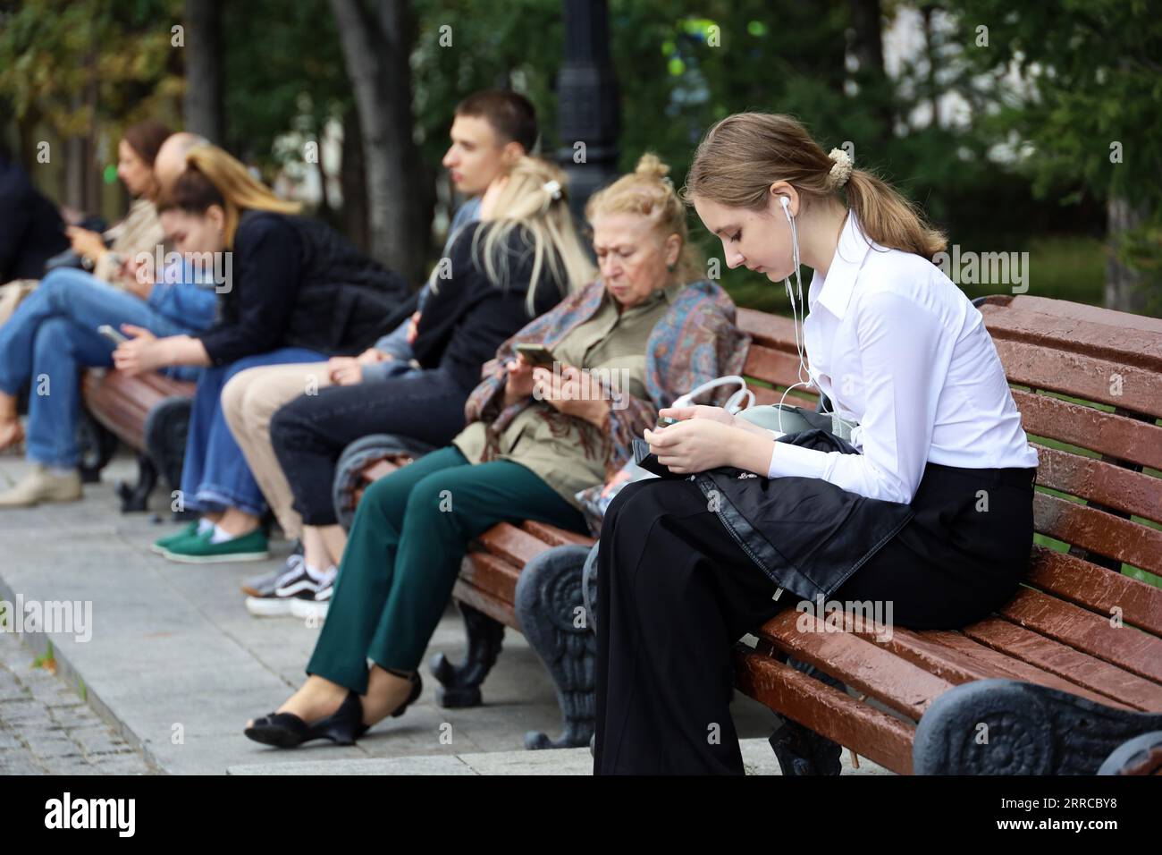 Personen, die Smartphones verwenden, sitzen auf der Straße der Stadt, mobile Kommunikation im Freien Stockfoto
