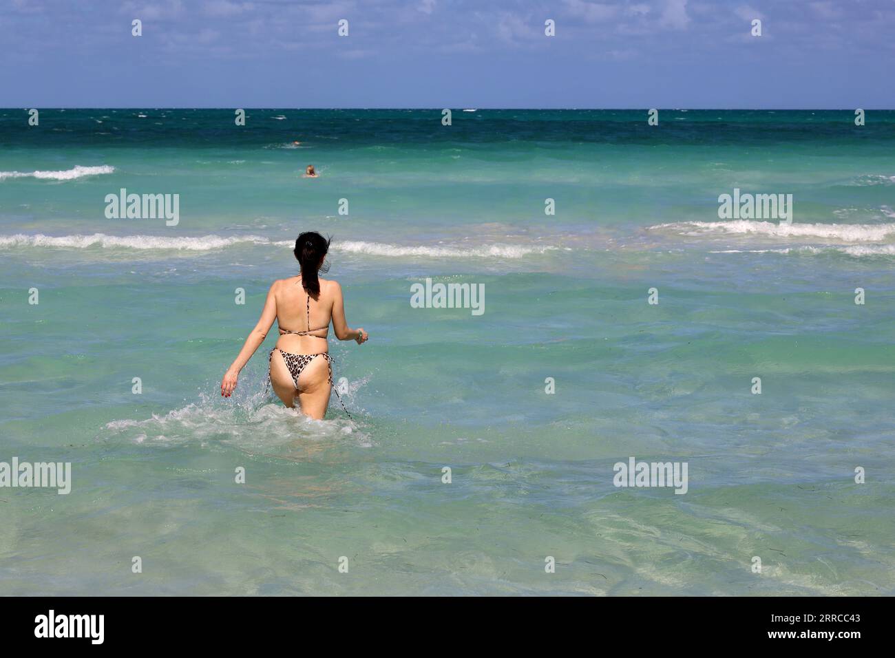 Frau im Bikini läuft in azurblauem Meerwasser. Strandurlaub an der sonnigen Küste Stockfoto