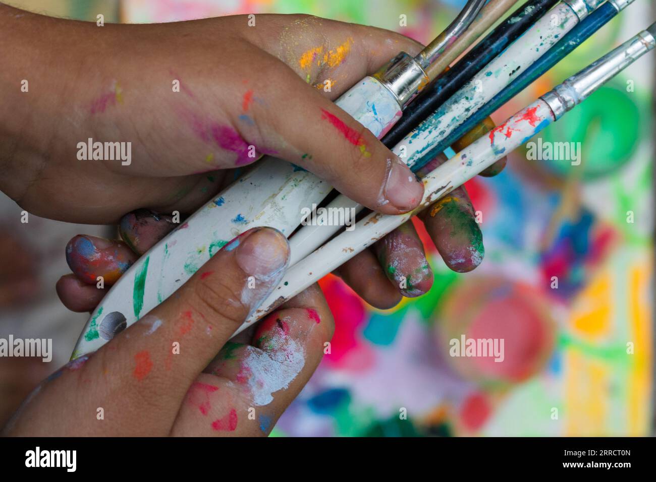 Das Hobby der Kinder ist das Malen. Hände mit Farbflecken schließen sich an, um Bürsten und Palettenmesser zu halten. Stockfoto