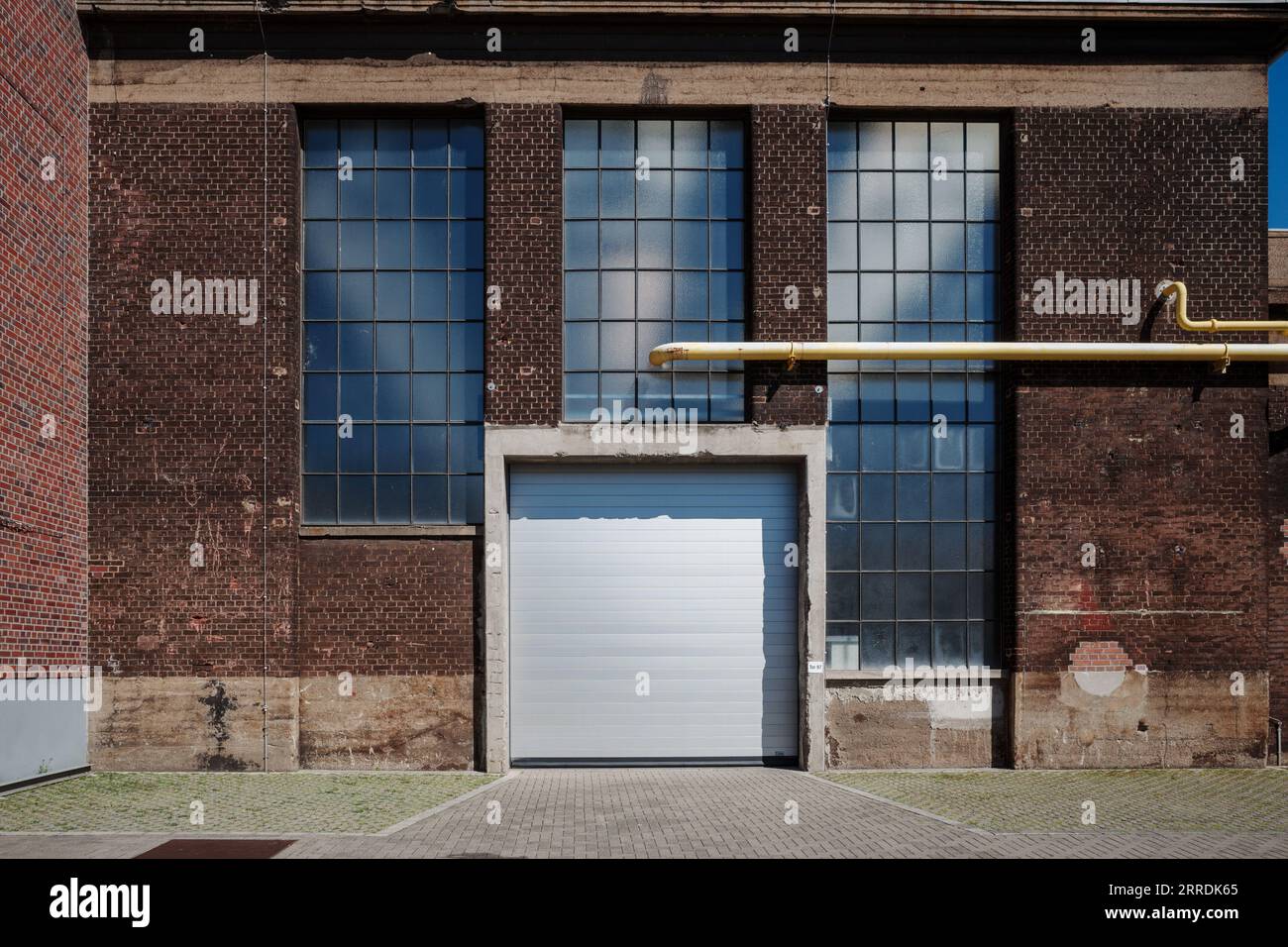 Außenansicht der Straße vor dem historischen Industriegebäude mit roter, alter Ziegelfassade, hohen Glasfenstern und weißem Metallverschluss. Stockfoto