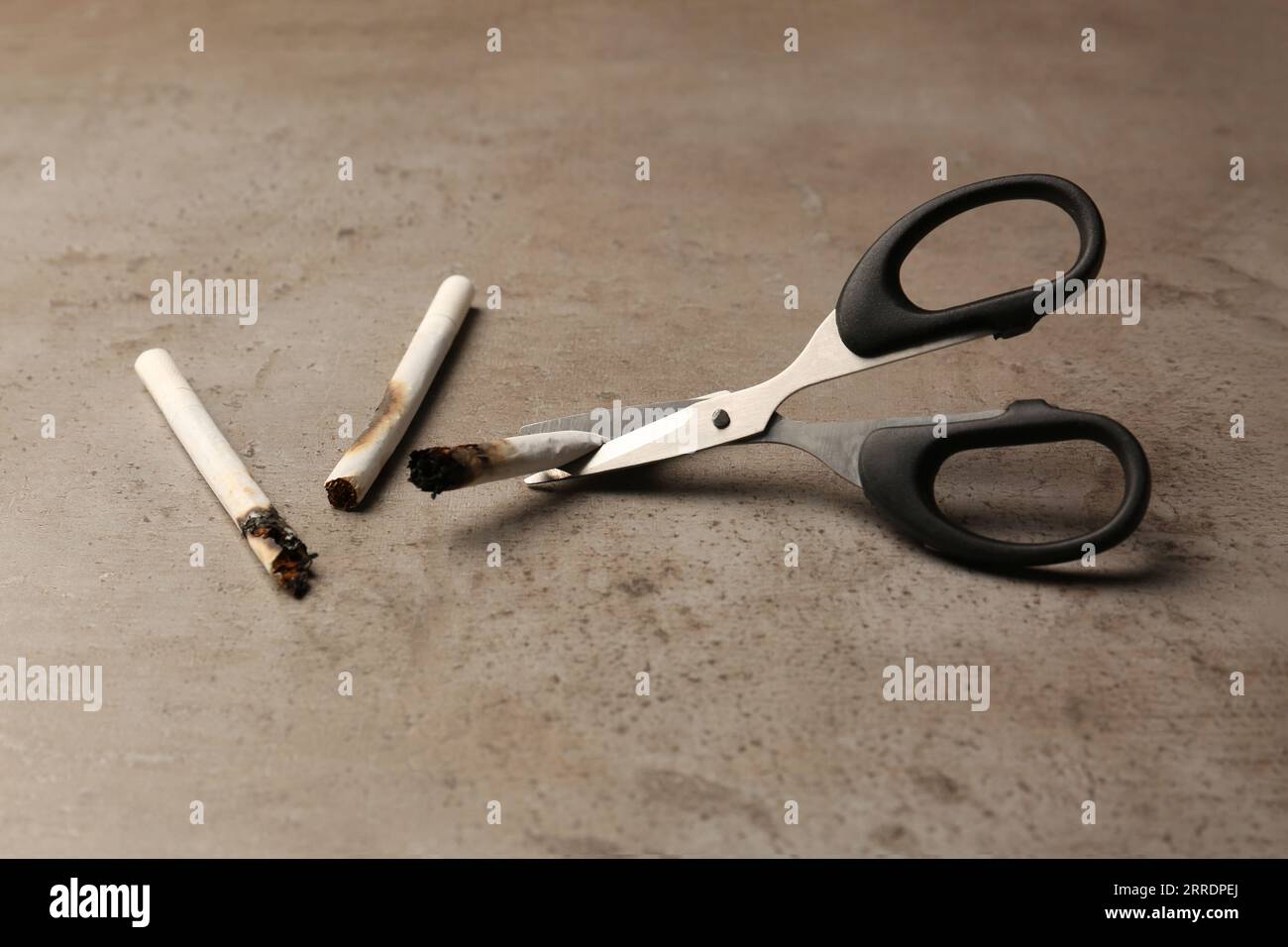 Schere zum Schneiden verbrannter Zigaretten auf grauem strukturiertem Tisch. Rauchverbot Stockfoto