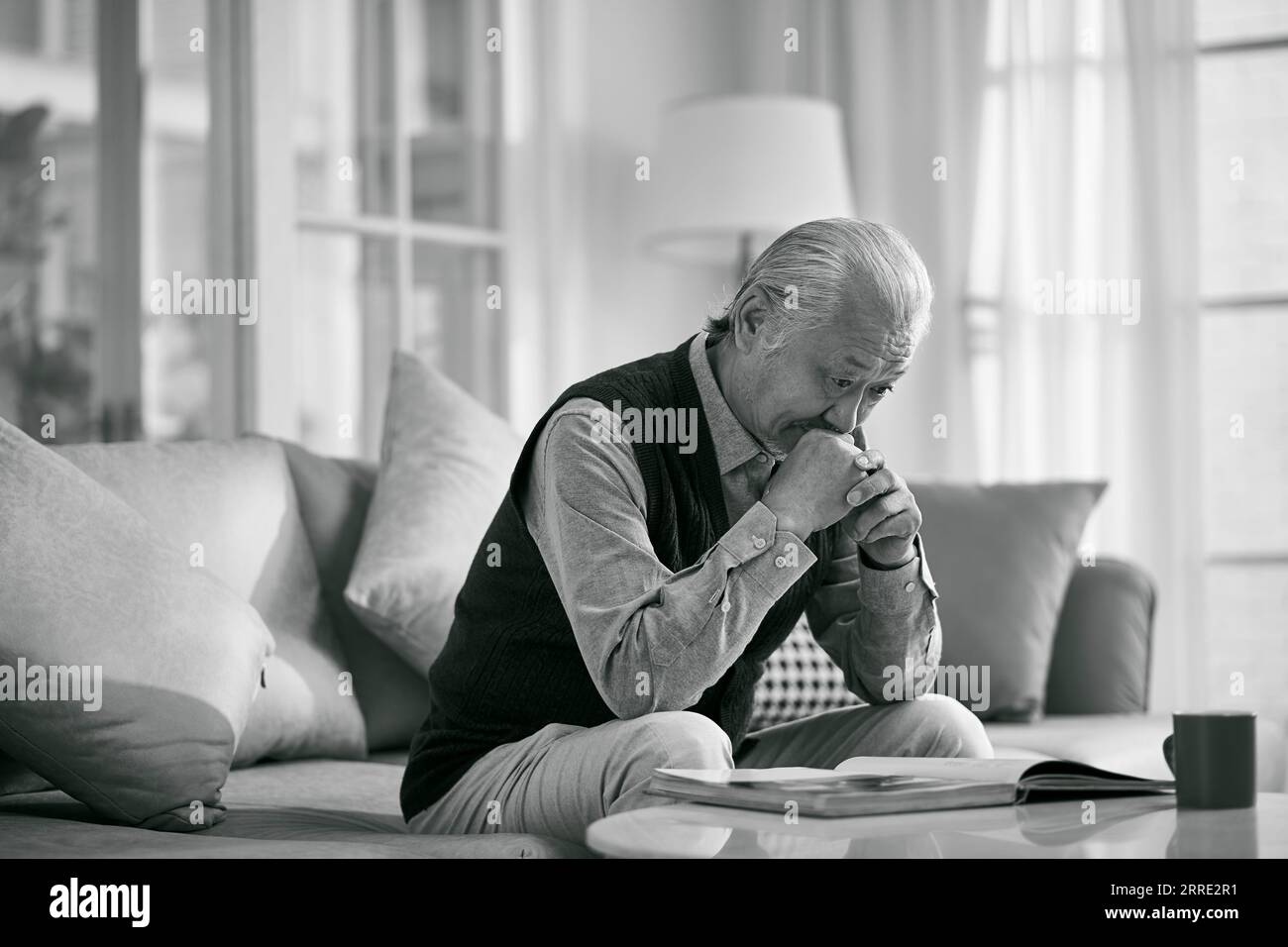 asiatischer Seniormann sitzt auf der Couch und denkt im Wohnzimmer zu Hause, schwarz-weiß Stockfoto