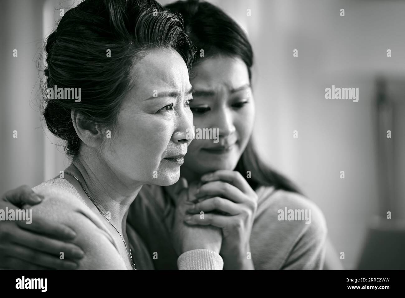 Traurige asiatische Seniormutter und erwachsene Tochter, die Hände hält, schwarz-weiß Stockfoto